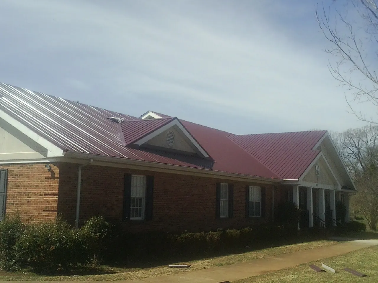 Red metal roof with gabled entries on a long brick building, from a Hail Damage Roof Repair job in Tiffin