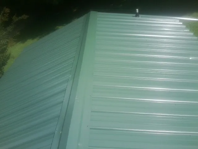 New green metal panels meeting at the ridge of a roof — Flat Roof Repair work by our crew in Tiffin