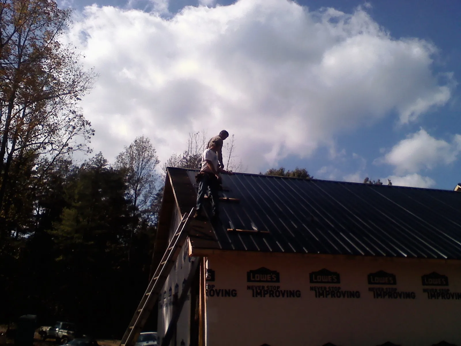 Roofer fastening dark metal panels high against a cloudy sky, from a Roof Inspection job in Tiffin
