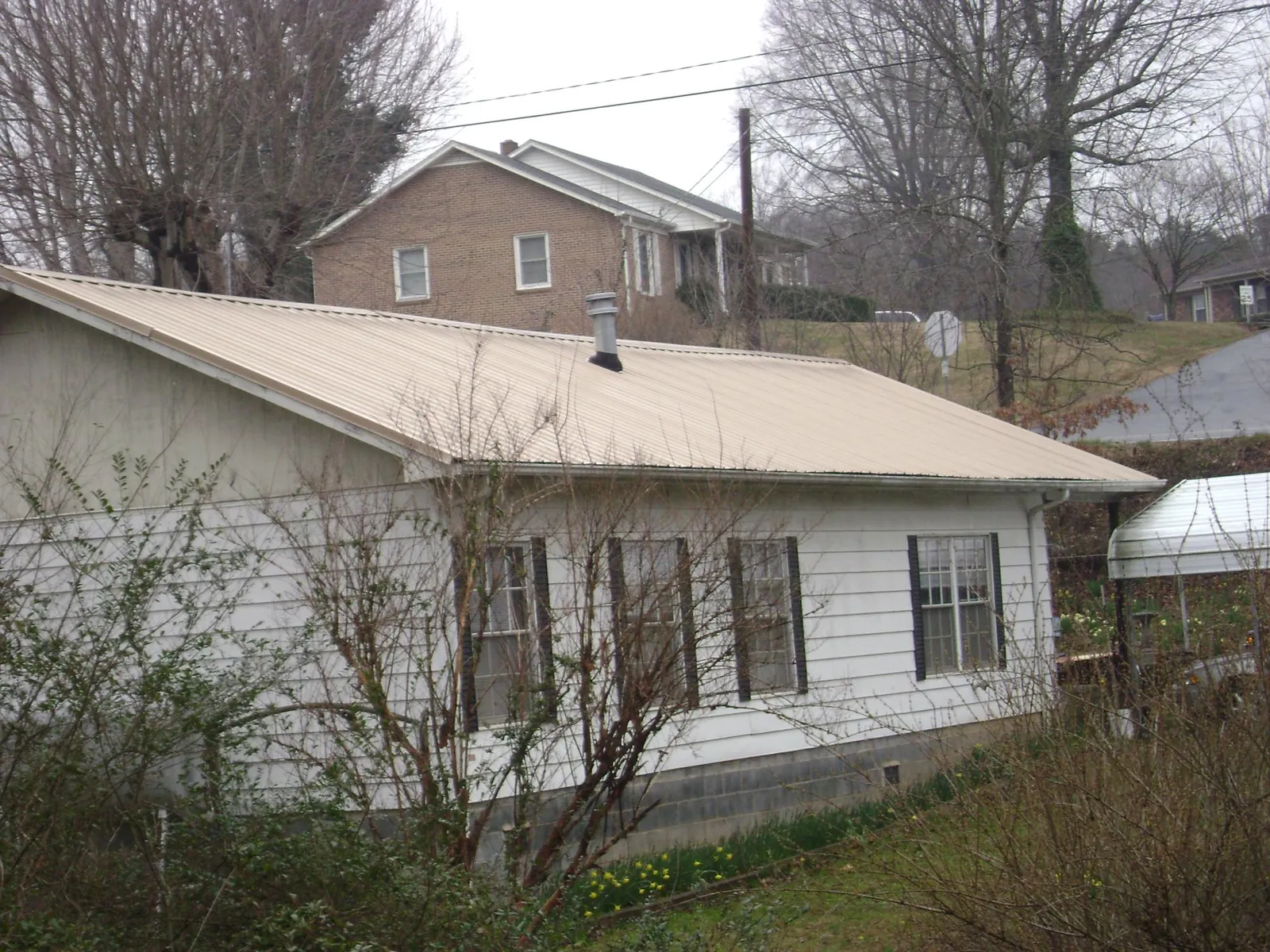 Tan metal roof on a white sided house set into a hillside — Commercial Roofing by Roofing Brothers in Tiffin